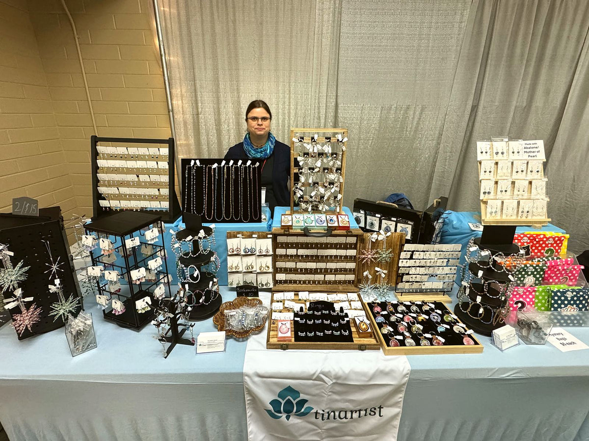 Tina behind her market table full of handmade beaded earrings, necklaces, keychains and snowflake ornaments